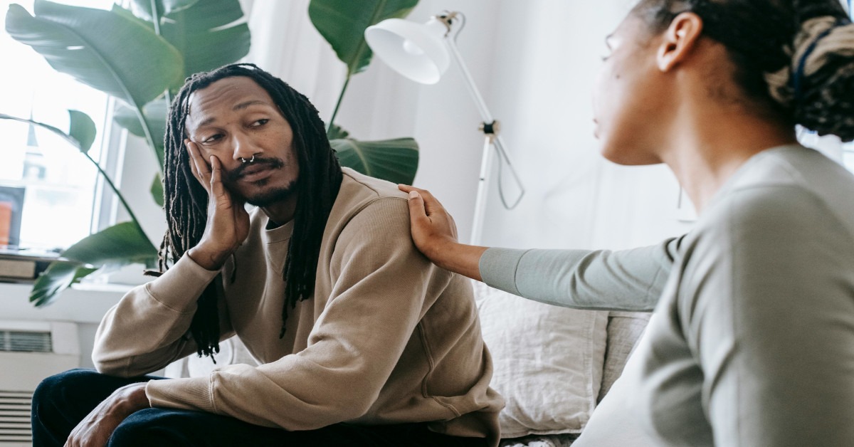 A counselor supporting a man by putting her hand on her shoulder.