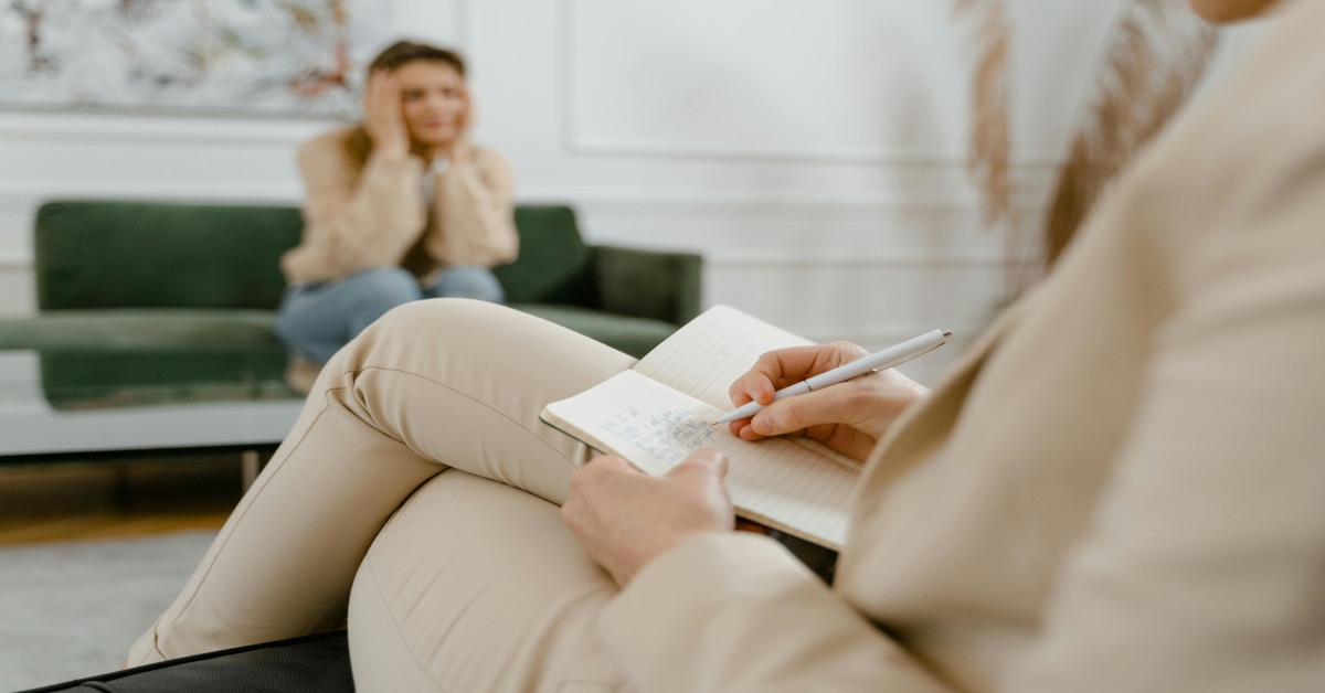 A therapist taking notes while sitting down and listening to her client.