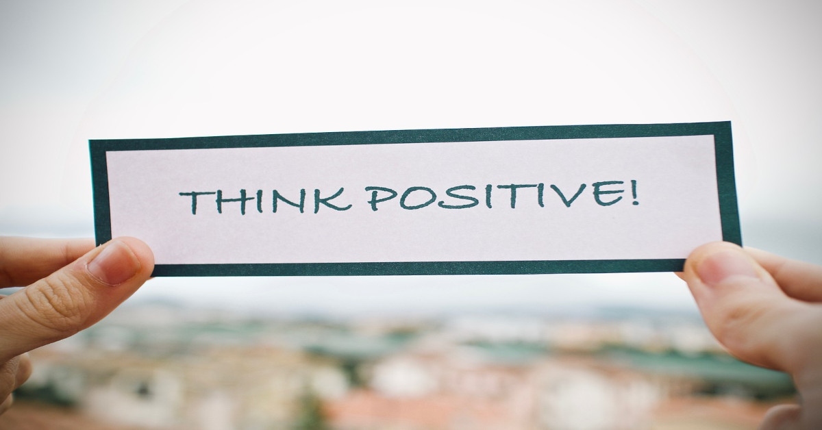 Someone's hands are holding a note saying, "think positive!"