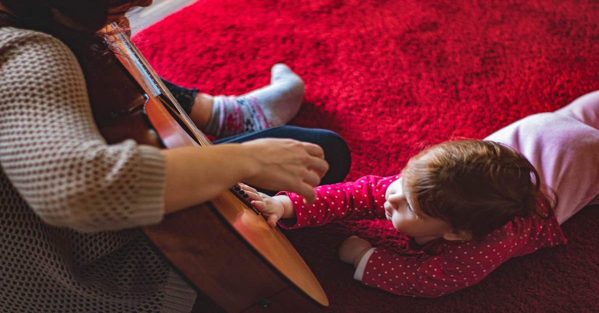 A toddler playing with the guitar of a woman.