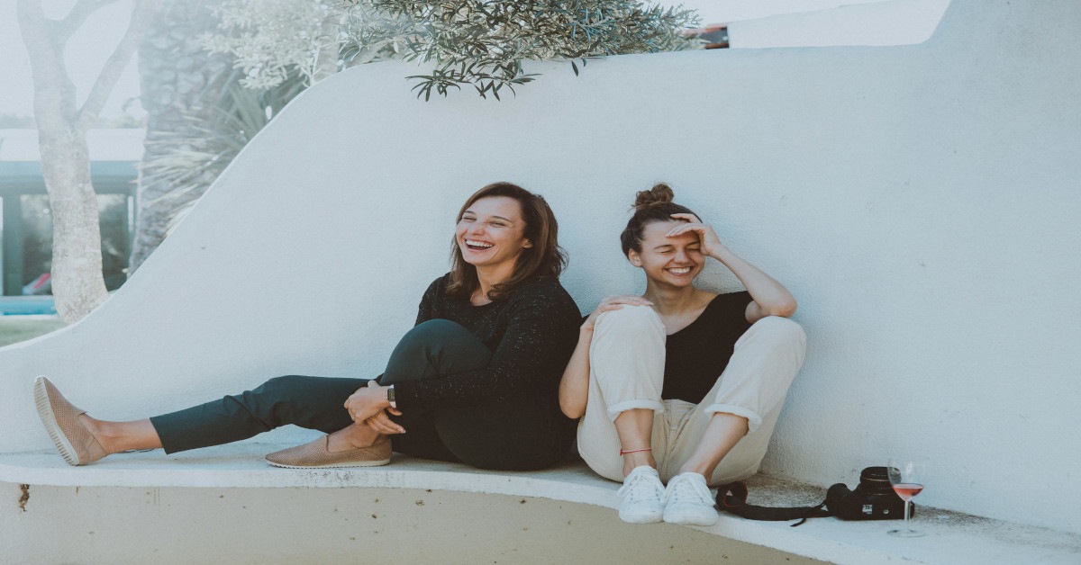 Two women sitting together outside while laughing.