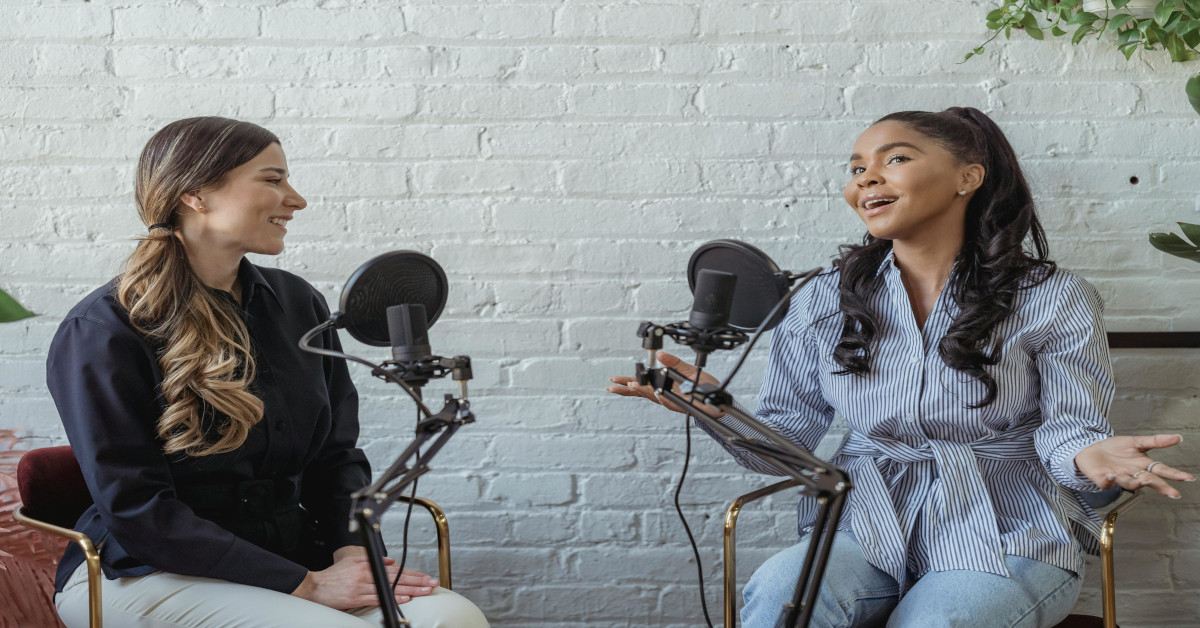 Two women podcasting while smiling.