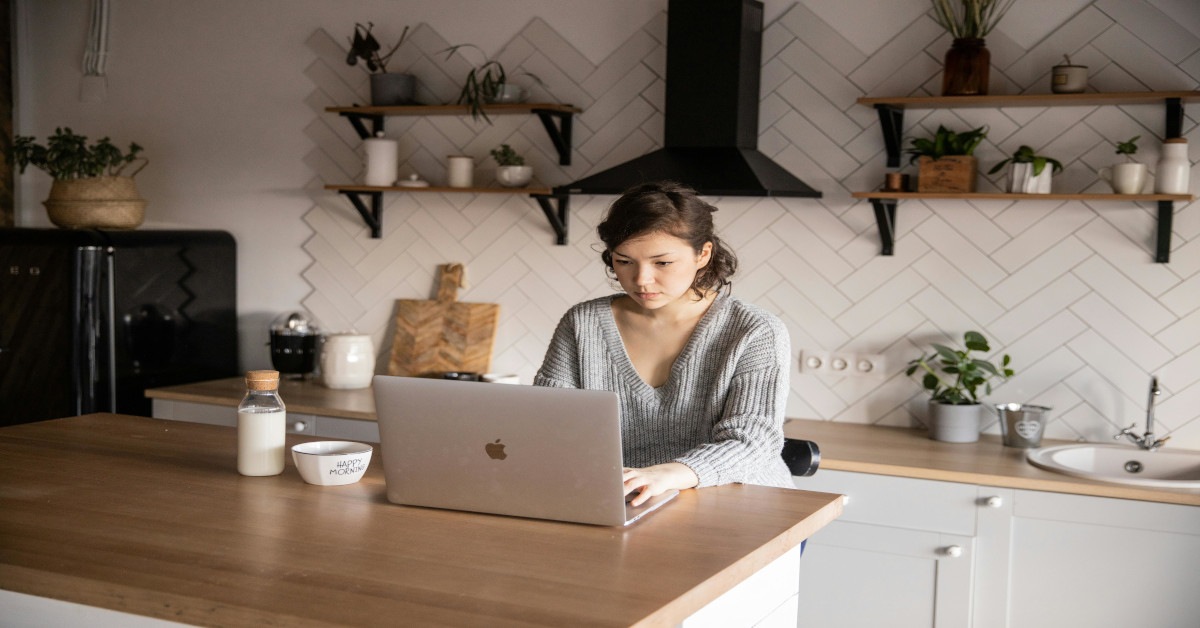 A woman browsing on a laptop while sitting in the kitchen.