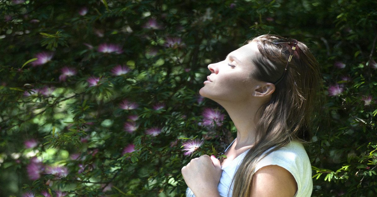 A woman smelling flowers outside while closing her eyes.