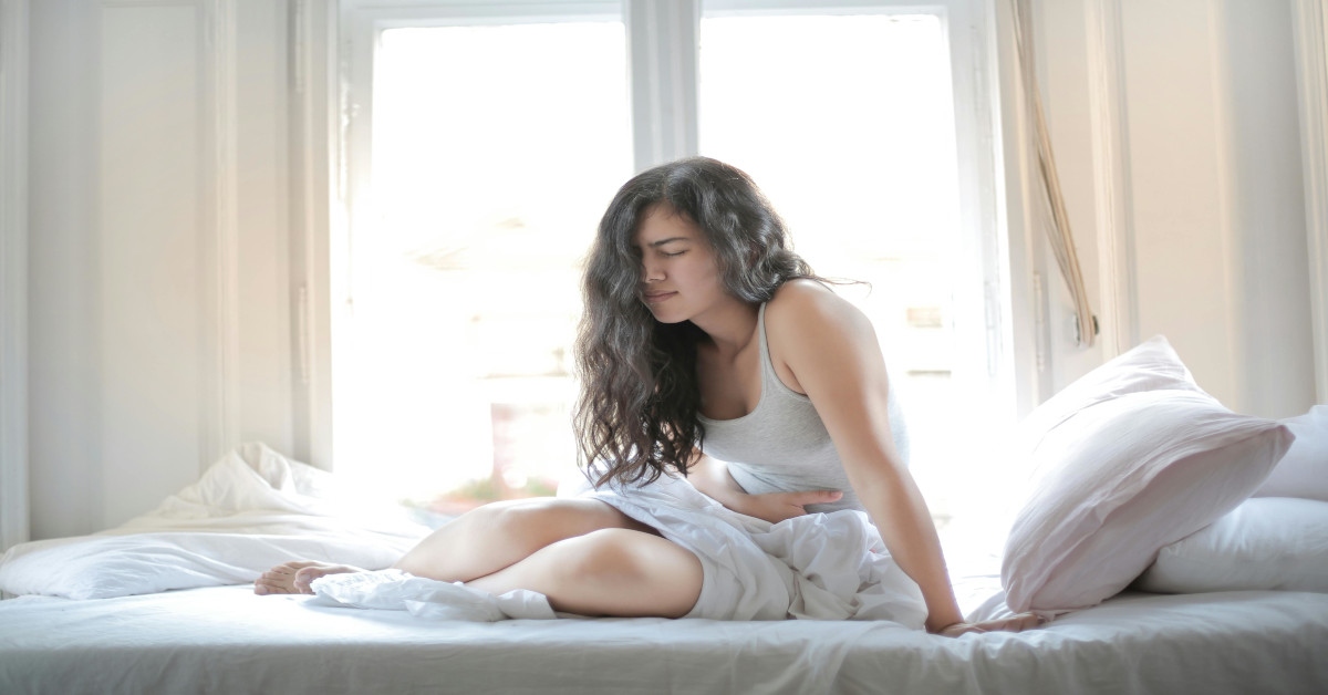 A woman holding her stomach in pain while sitting in bed.