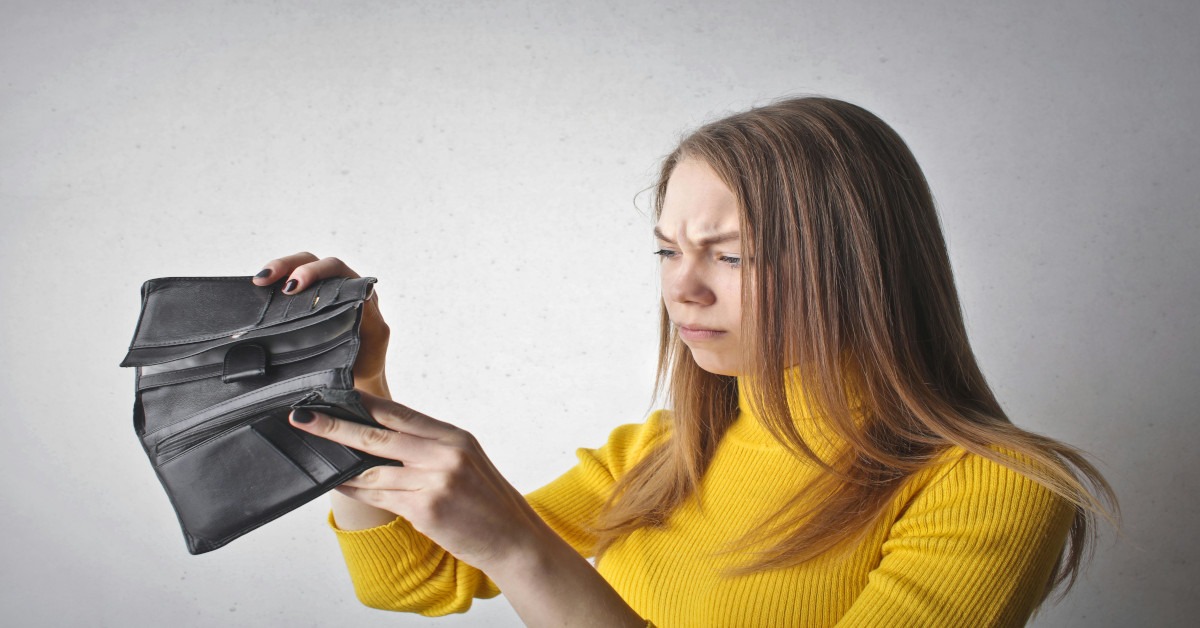 A young woman is looking concerned while holding a black wallet that's empty, indicating that she's having financial troubles.