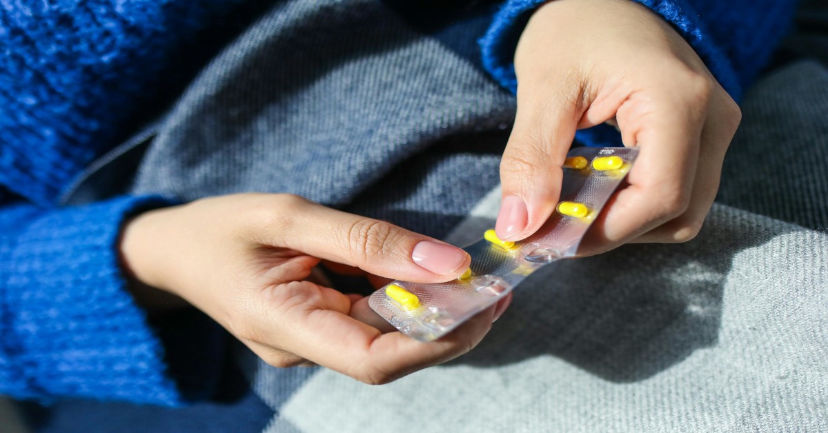 A woman holding a strip of yellow medication.