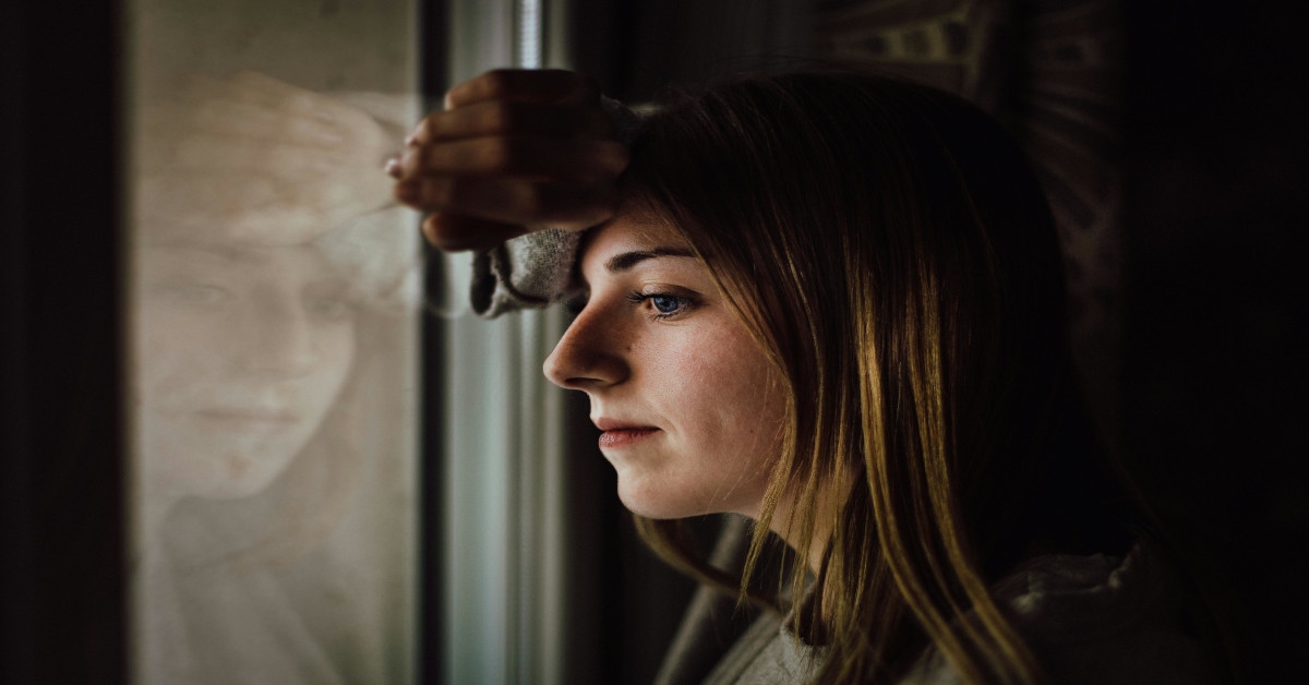 A woman is leaning against a glass window while thinking.