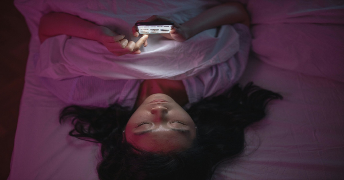 A woman lying in bed and scrolling on her phone.