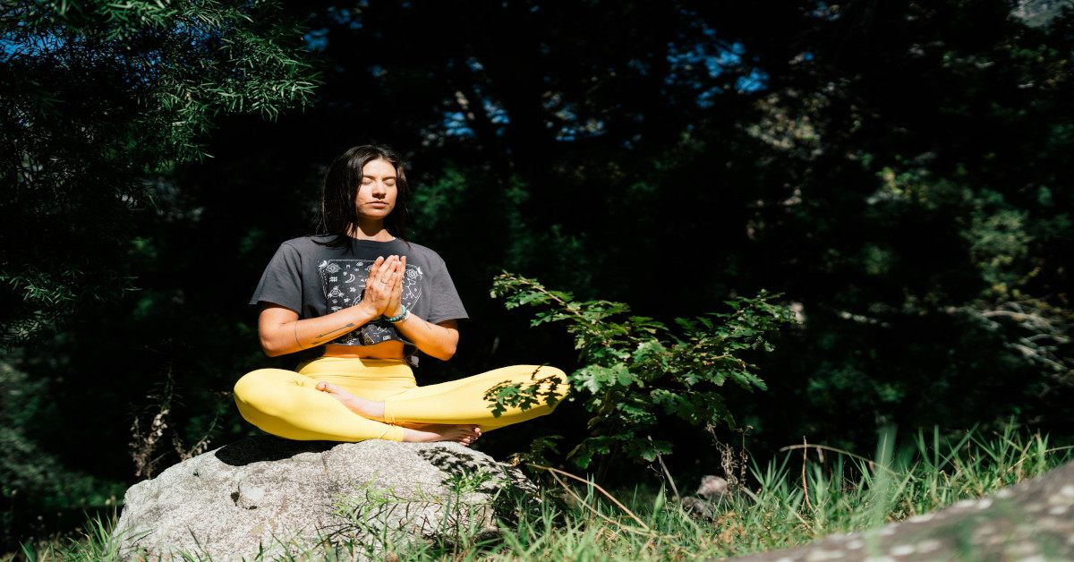 A woman practicing mindfulness while sitting on a rock.