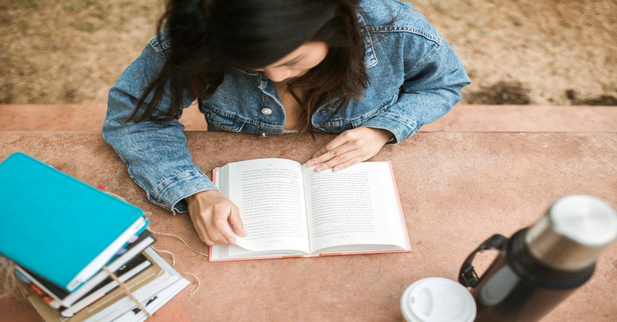 A woman reading a book on a table outside.
