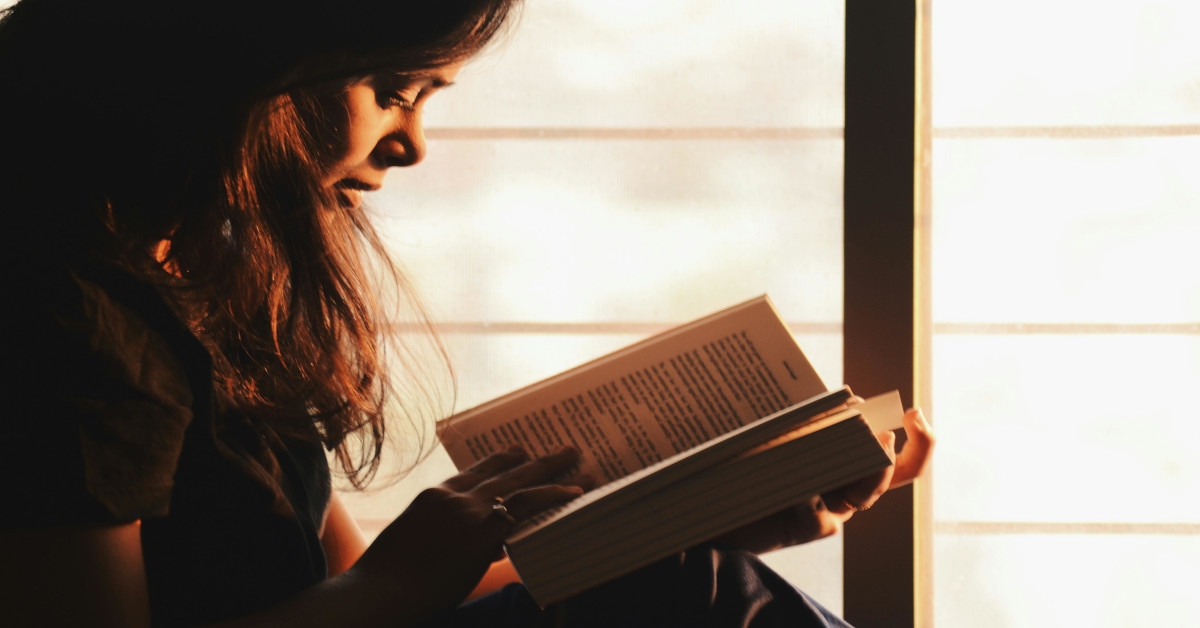 A woman reading a book next to a window.