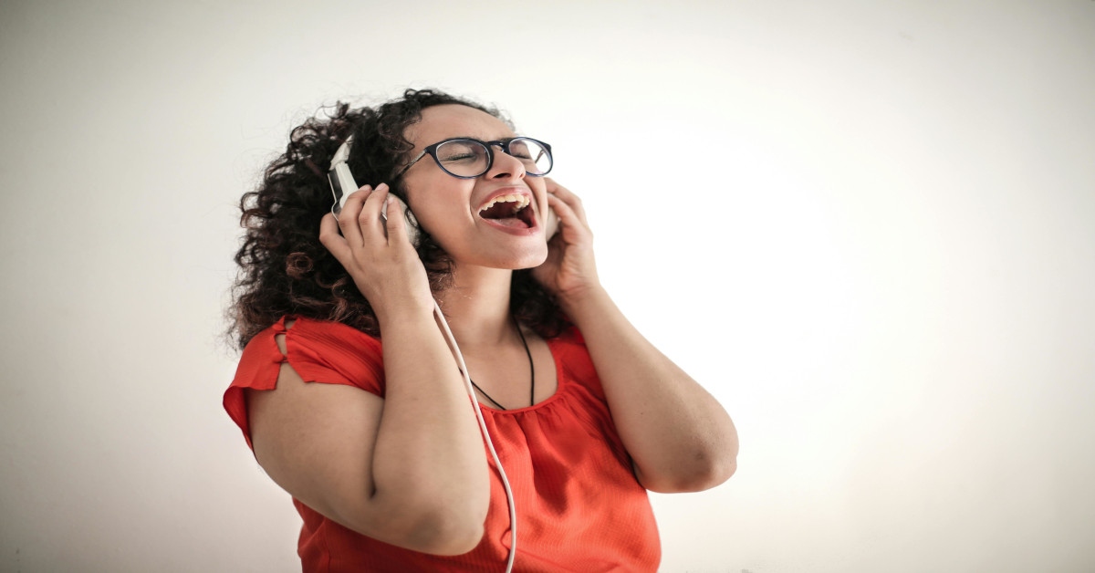 A woman with a red shirt singing while wearing headphones.