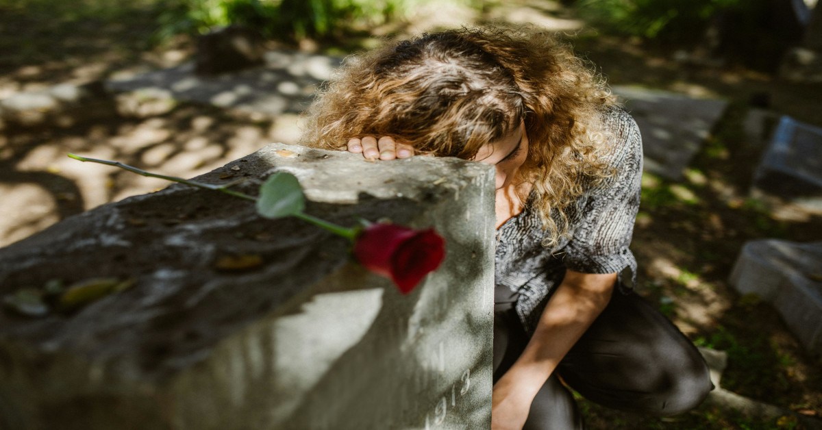 A woman who is sad while holding a grave while kneeling down.