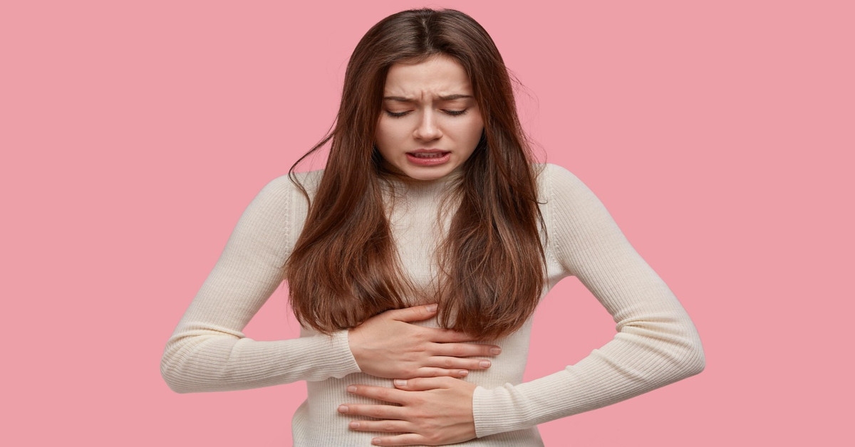 A woman holding her stomach in pain with a pink background.