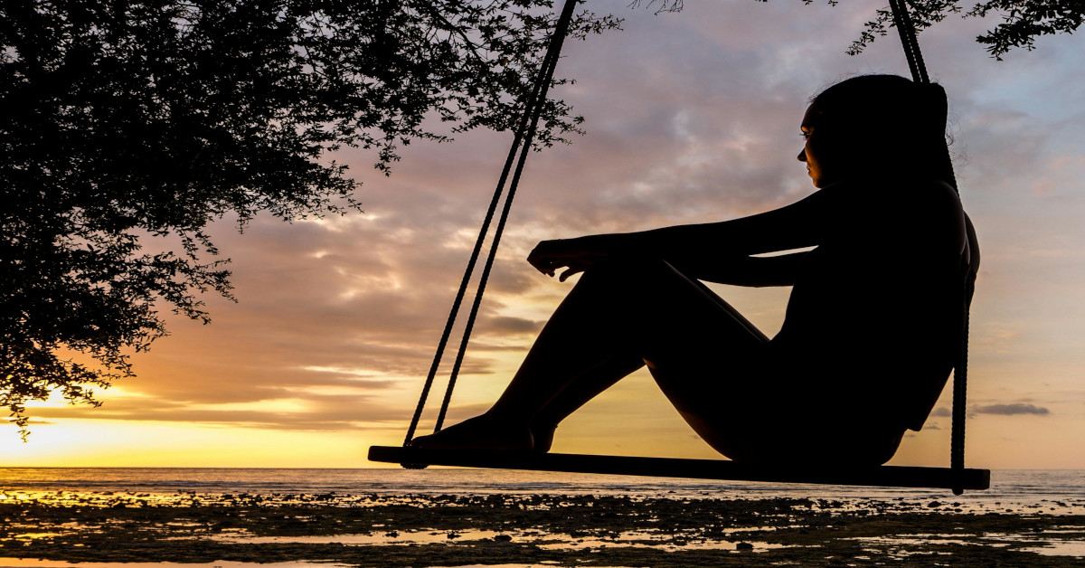 A woman is thinking while sitting on a swing.