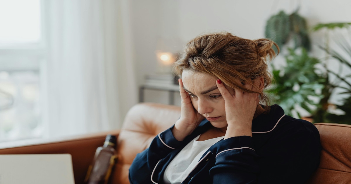 A woman holding her head while sitting in a couch.