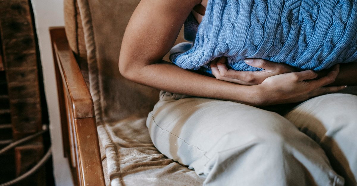A woman sitting down while holding her stomach, indicating that she has stomach pain.