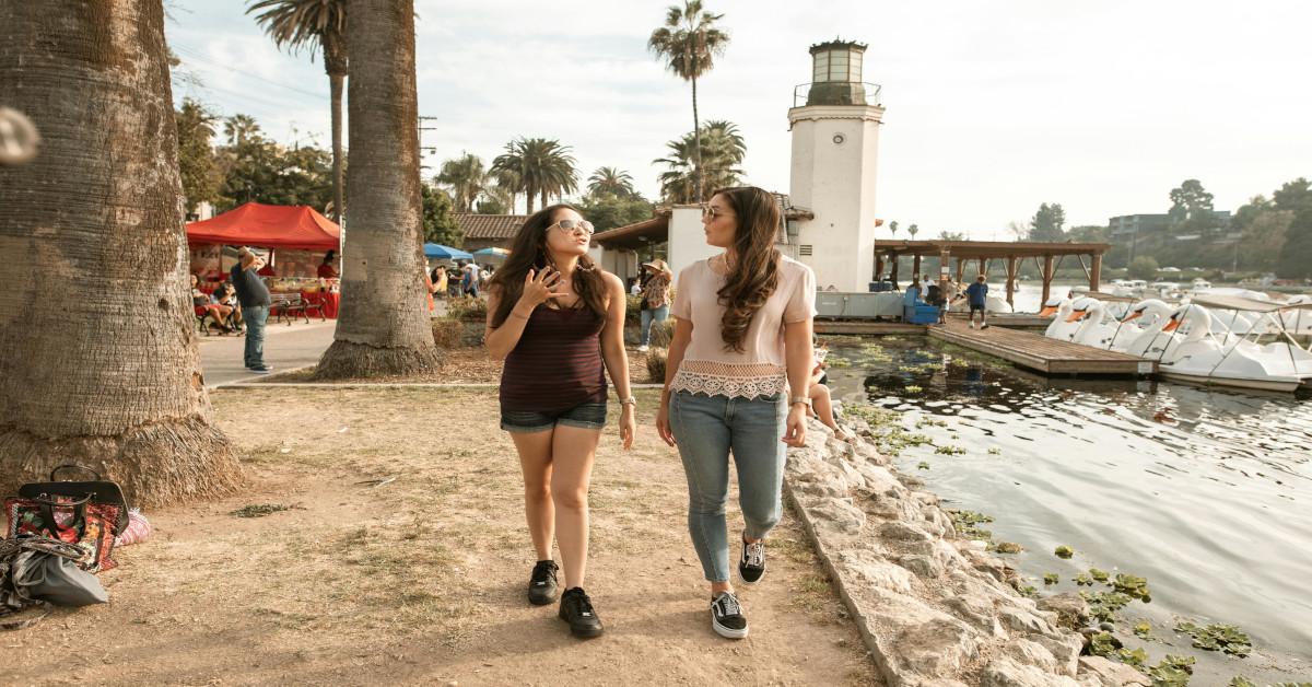 Two women walking and talking near a lake.