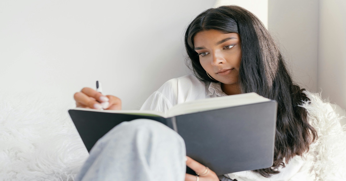 A woman writing in a workbook while sitting down.