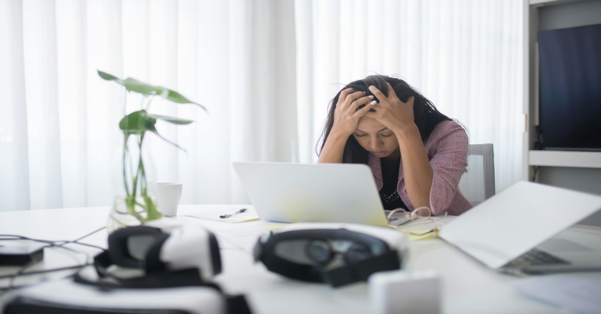 Woman holding her head in front of a laptop at work, indicating she's stressed out.