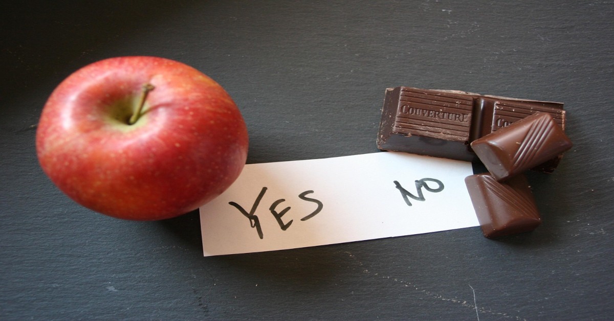 Image showing an apple with the word "yes" written on a piece of paper on the left and a chocolate with the word "no" written on a piece of paper on the right, indicating that we should eat healthier.