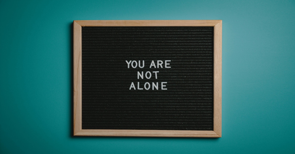 The sentence, "you are not alone," written in white letters on a black background with a wooden frame.