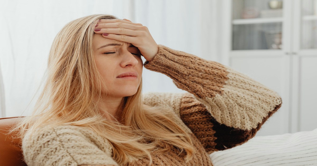 A young blonde woman holding her head.