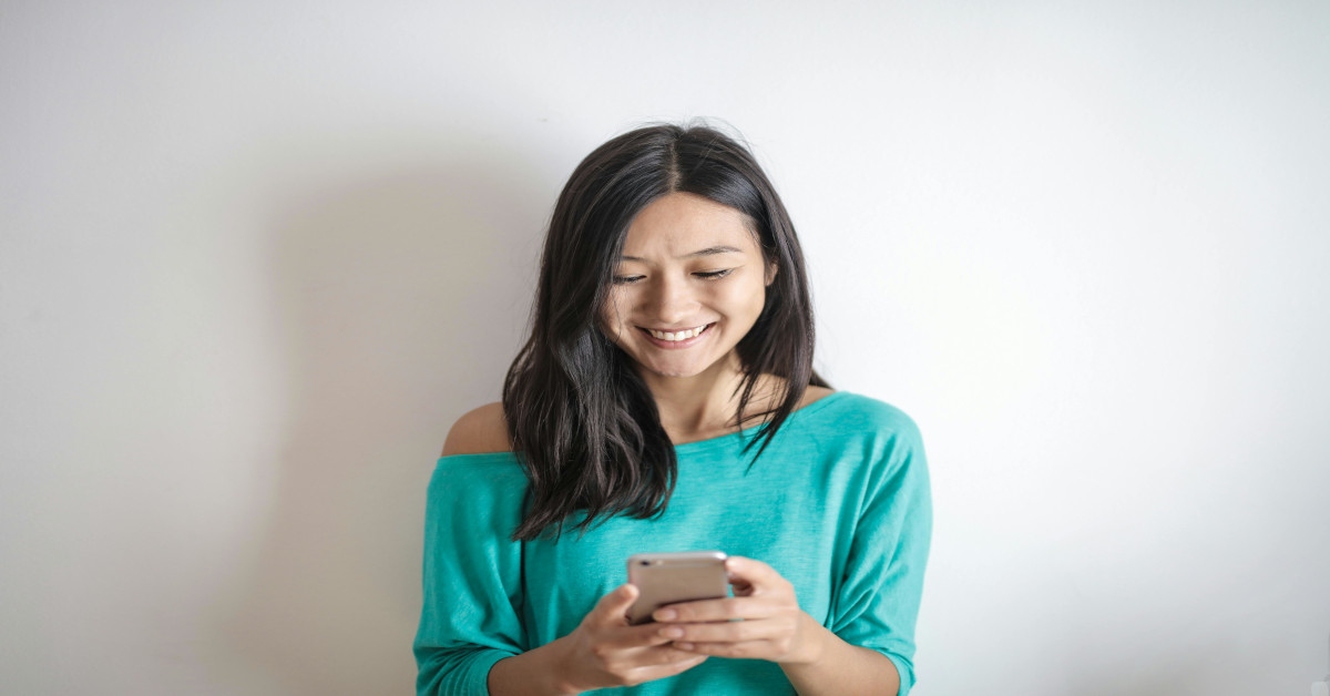 A young woman sending a text while smiling.