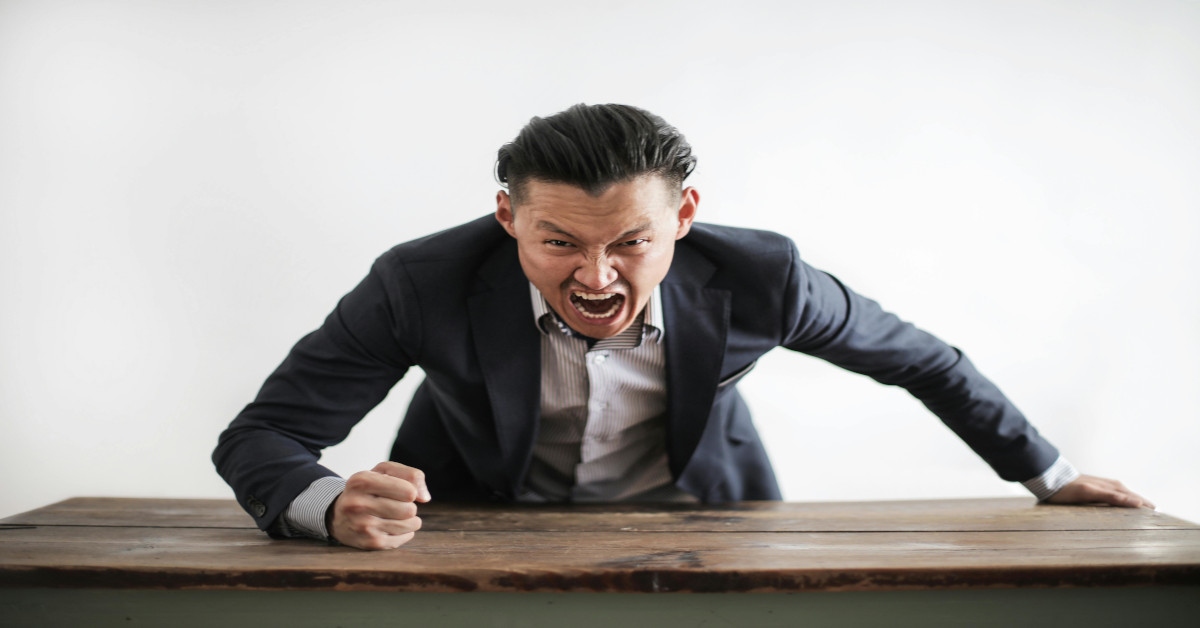 An angry man yelling while pounding his fist on a table.