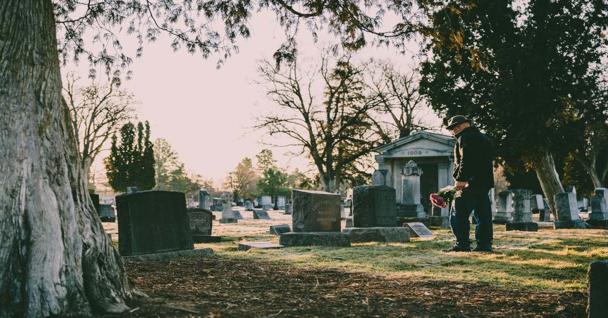 A man standing at a funeral with roses.