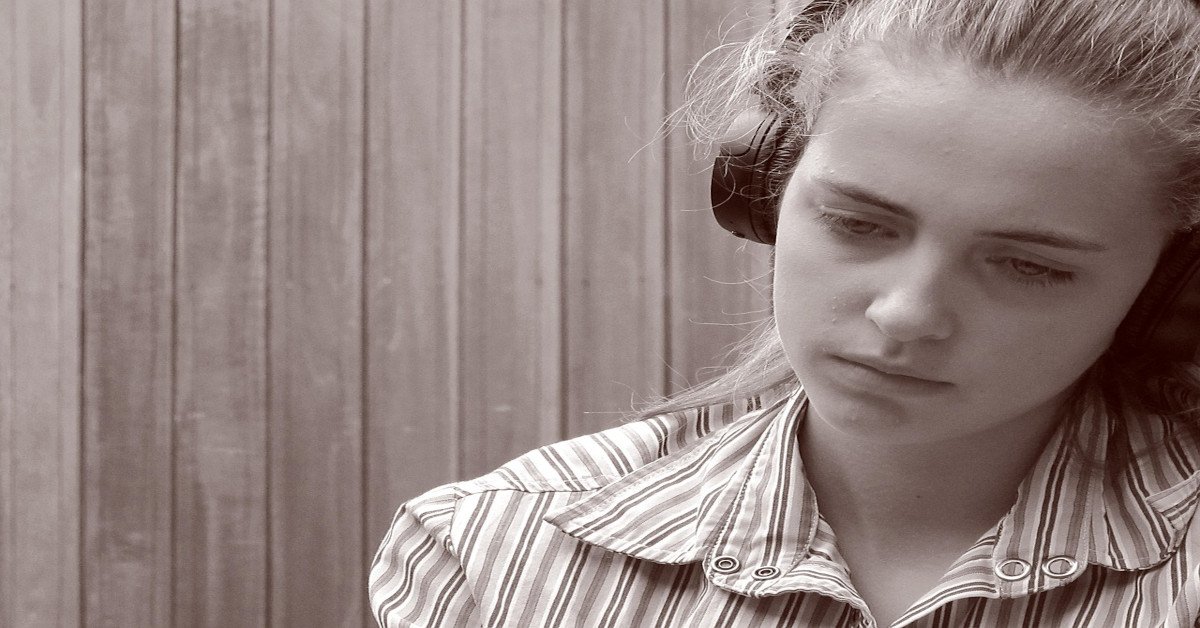 A young woman is listening to music with a blank stare.