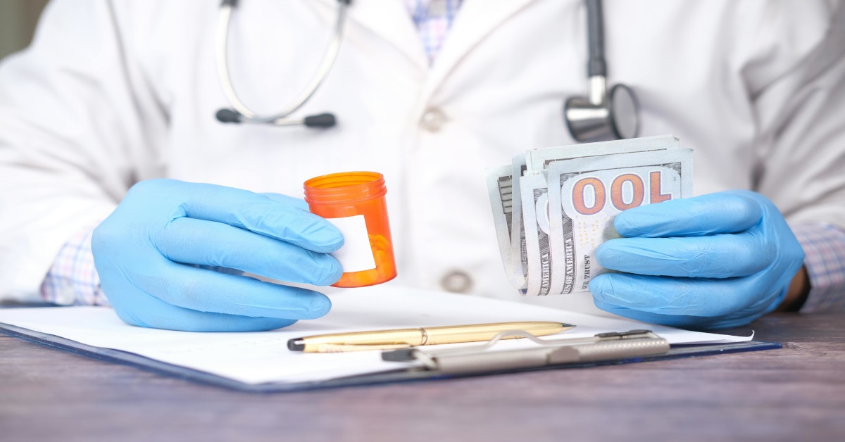 A healthcare professional holding a bottle of pills in one hand and money in the other, indicating that it costs money.