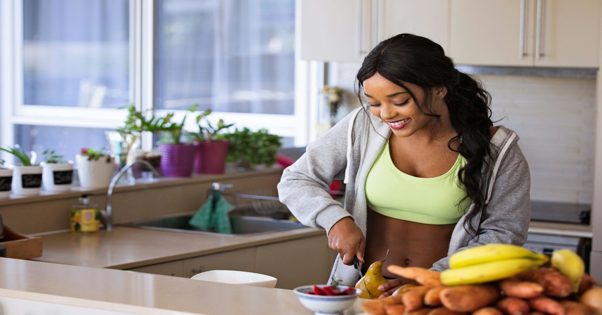 Image of a fit black woman cutting fruit while smiling.
