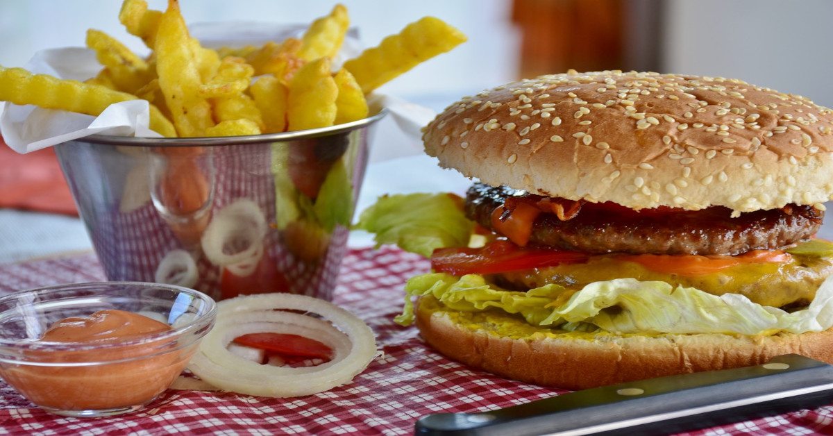 A hamburger and french fries resting on a plate on the table.