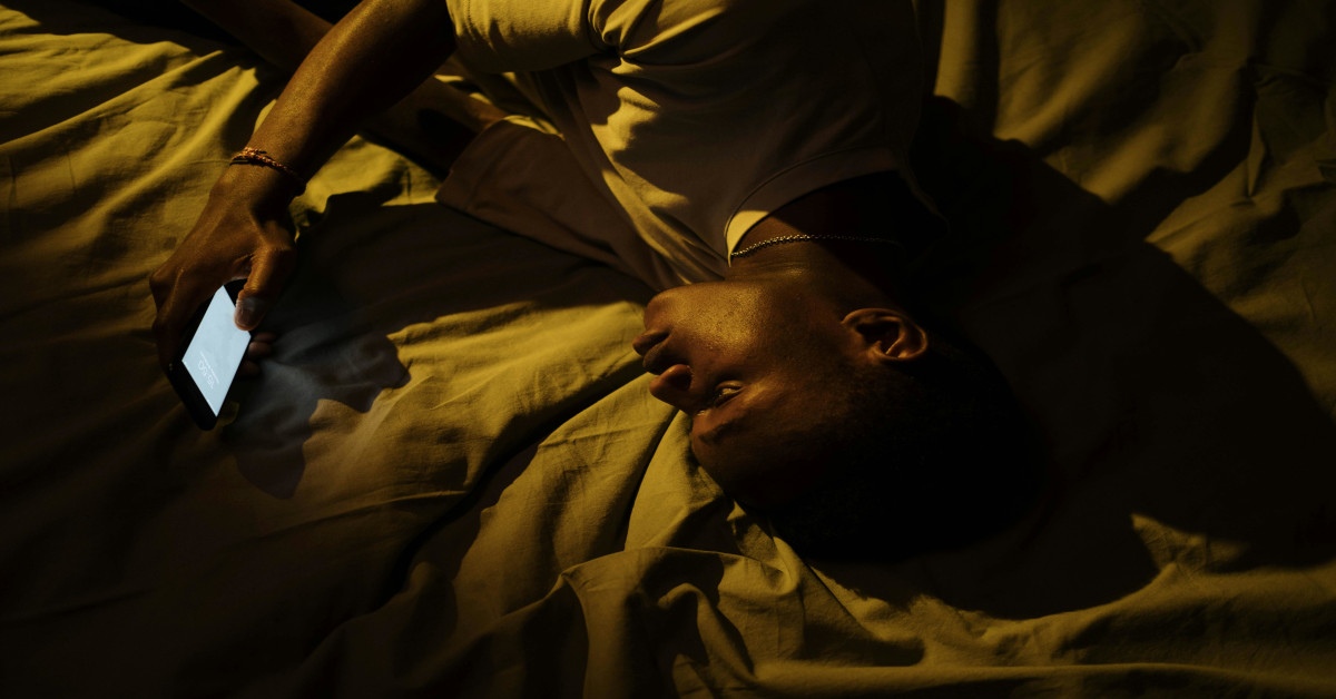 A man lying awake in his bed and using his phone.