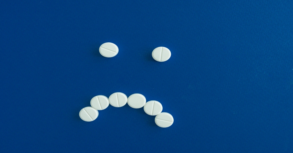 Image of medication forming a sad smiley face on a blue background.