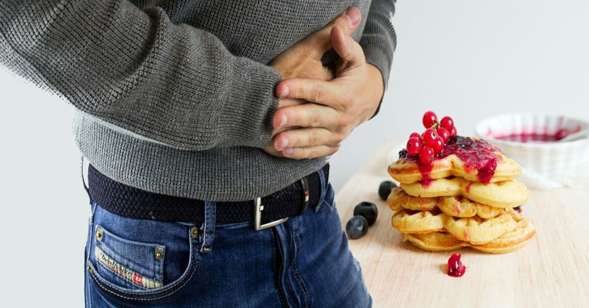 A man grabbing his stomach in pain from overeating.