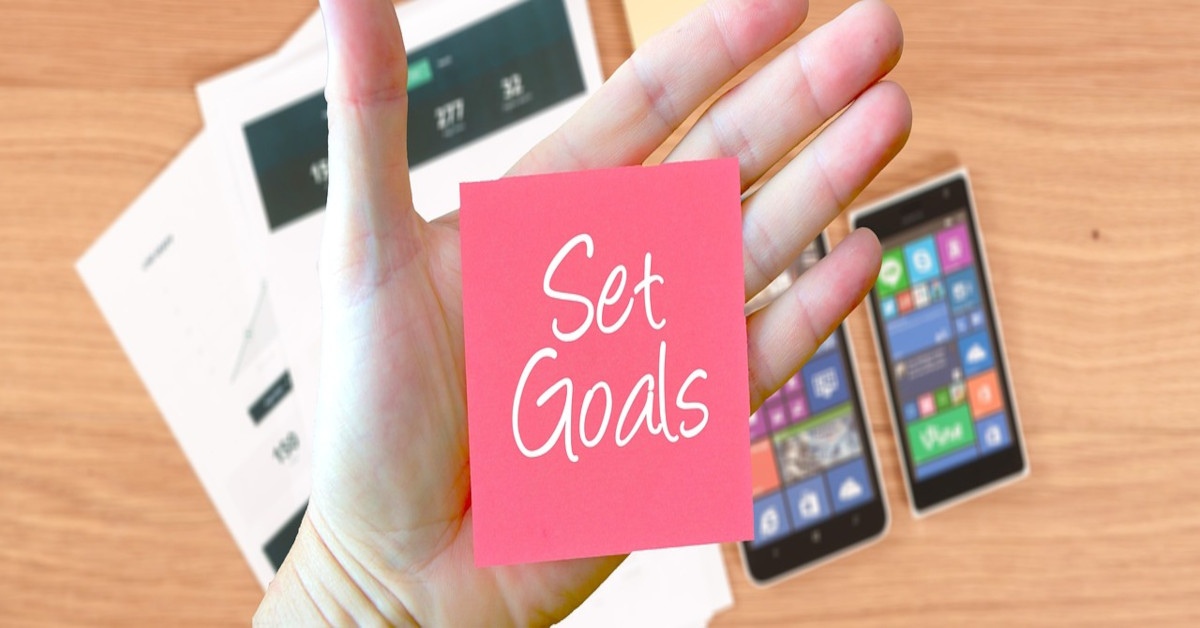 Image of someone's hand holding a red post-it note reading, "set goals".
