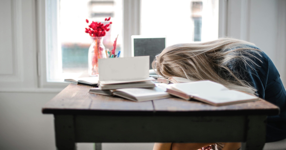 A woman lying with her face on the table in between books, indicating that she's stressed out and tired.