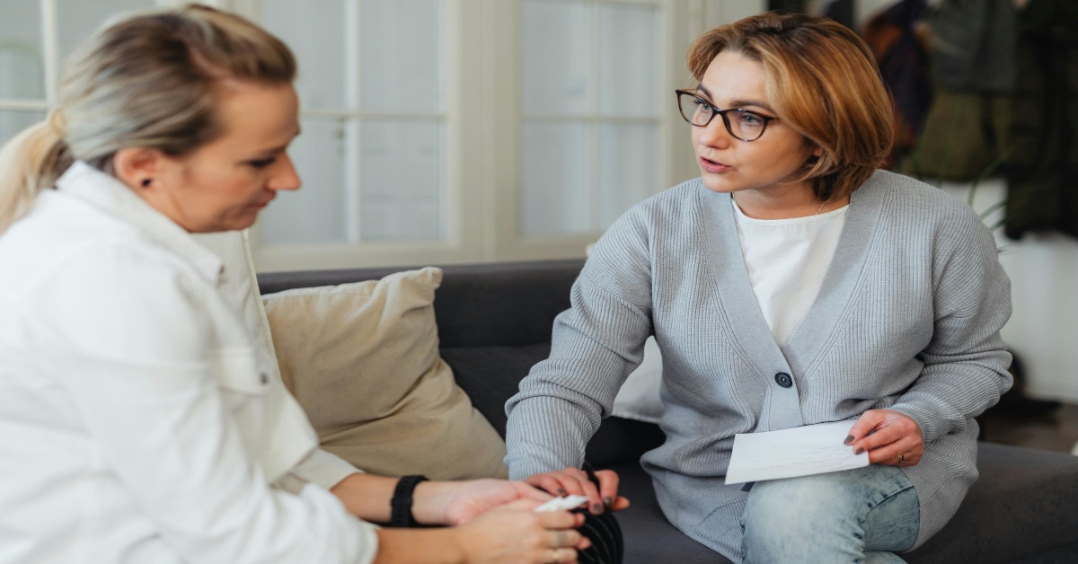 A counselor talking to a client while putting her hand on her lap in support.