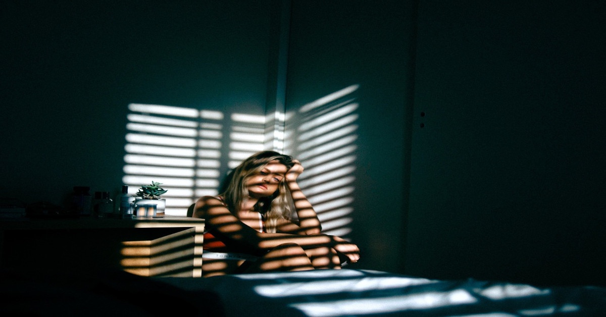 A woman sitting alone at home, seemingly bored while holding her head.