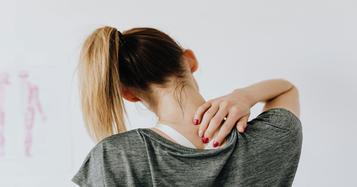 A woman holding her neck while bending it, seemingly being in pain.
