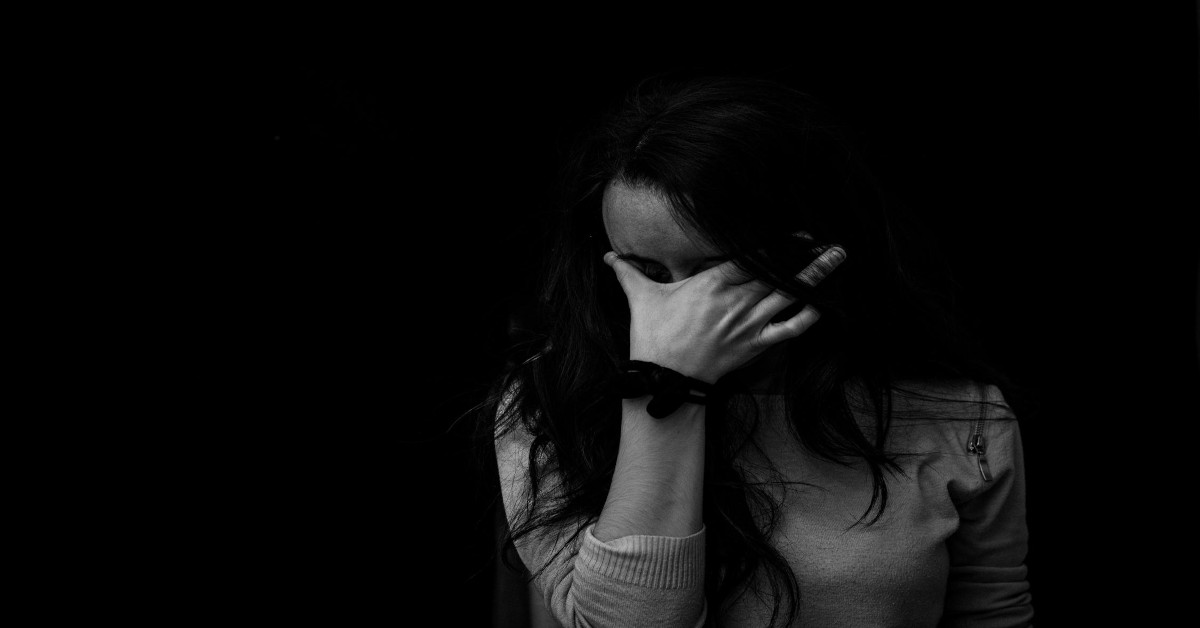 A woman holding her head and surrounded by darkness, indicating that she's depressed.